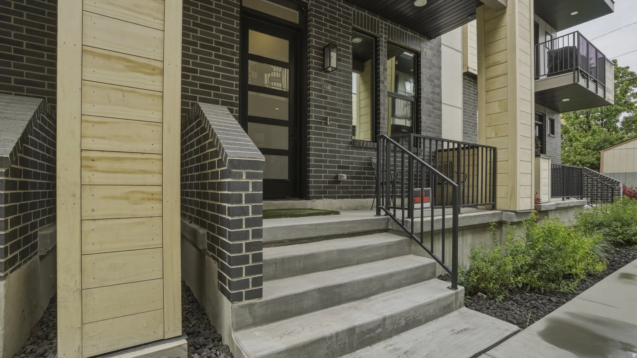Modern multi-level exterior with dark brickwork, light wood-finish siding, and a black-framed entry door with frosted glass panels