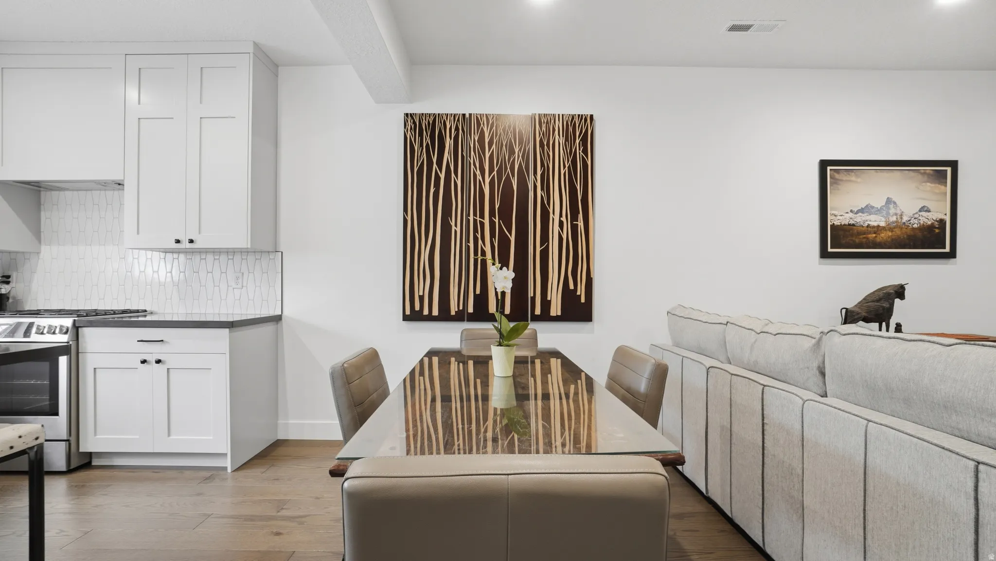 Open-concept living space with wood-finish flooring, white cabinetry, dark countertops, and a full tile backsplash