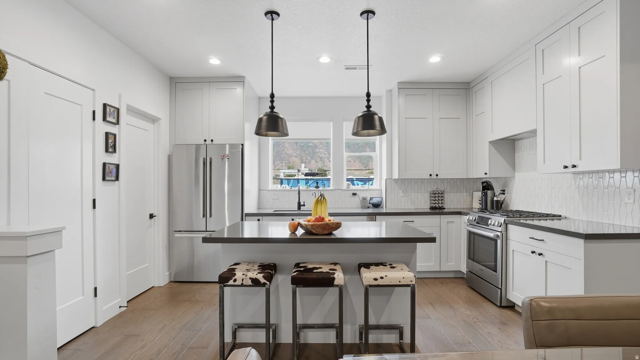 Modern kitchen featuring white shaker cabinetry, stainless steel appliances, dark countertops, and a central island with pendant lighting