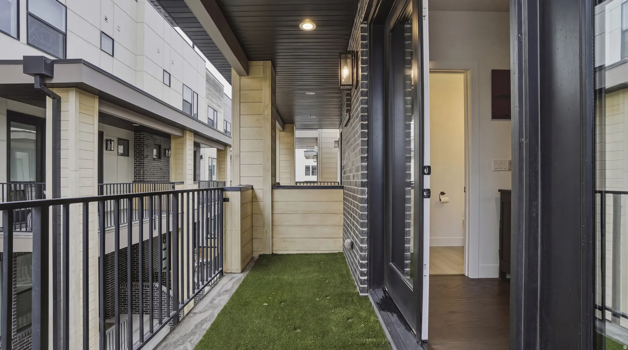 Outdoor balcony featuring artificial turf flooring, black metal railings, and a black brick exterior wall