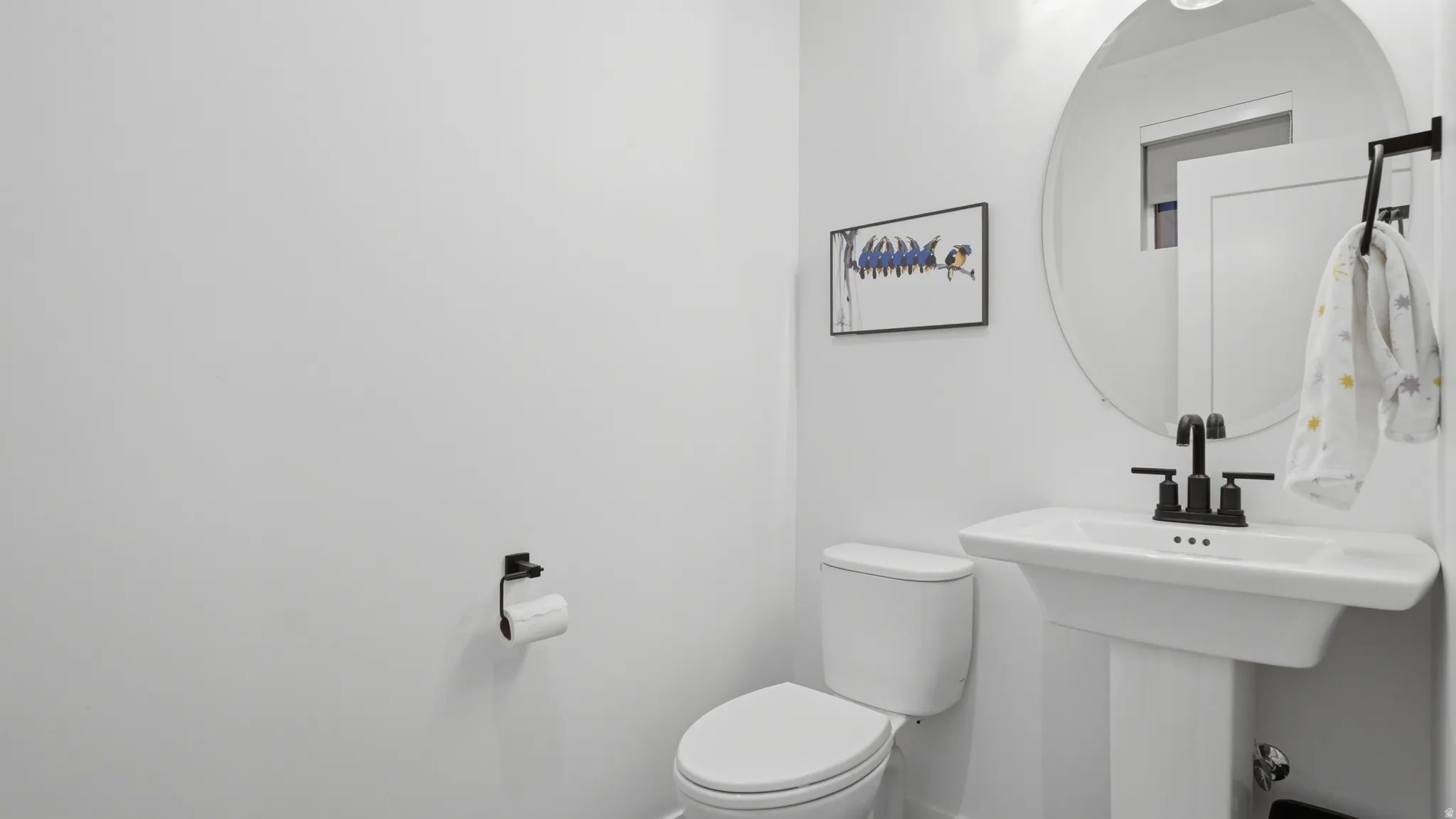 Pedestal sink with matte black faucet, wall-mounted circular mirror, and recessed lighting