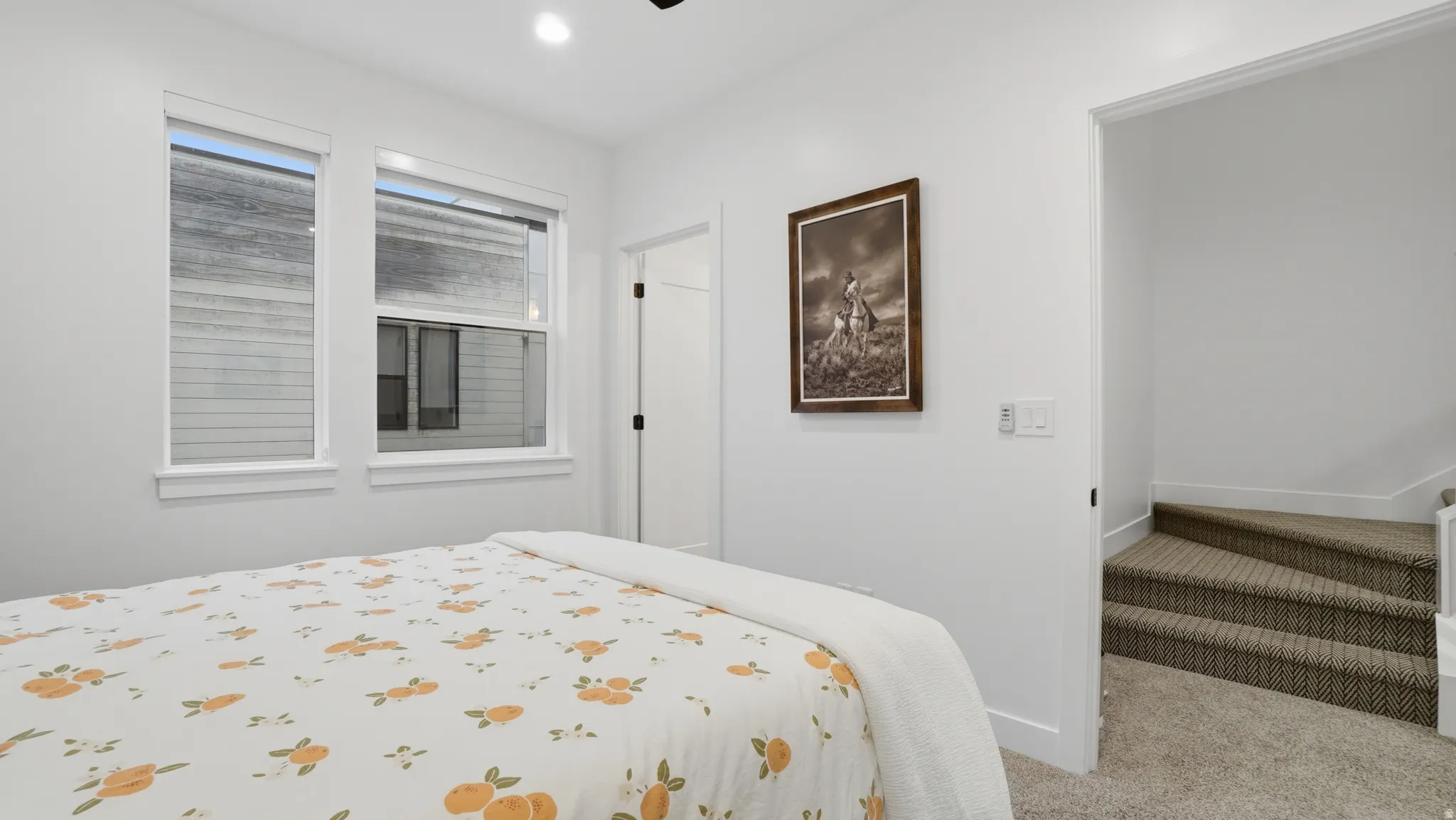 Bright interior space featuring two windows with white trim, recessed lighting, a paneled door with black hardware, white walls, and textured carpeted stairs