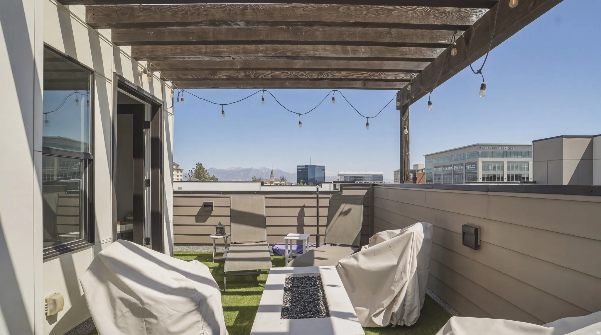 Rooftop patio featuring a wooden pergola with string lighting, faux turf flooring, a built-in fire pit, and a sliding glass door entry