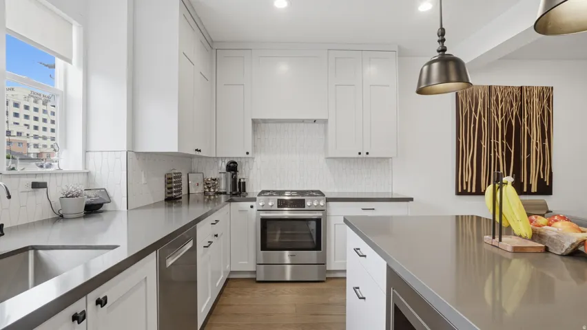 Modern kitchen featuring white shaker cabinetry, stainless steel appliances, a tile backsplash, dark countertops, and wood-finish flooring