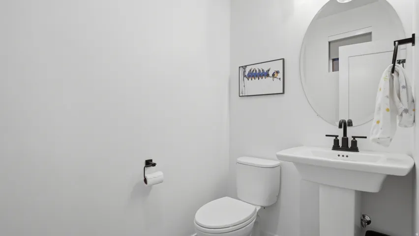 Pedestal sink with matte black faucet, wall-mounted circular mirror, and recessed lighting
