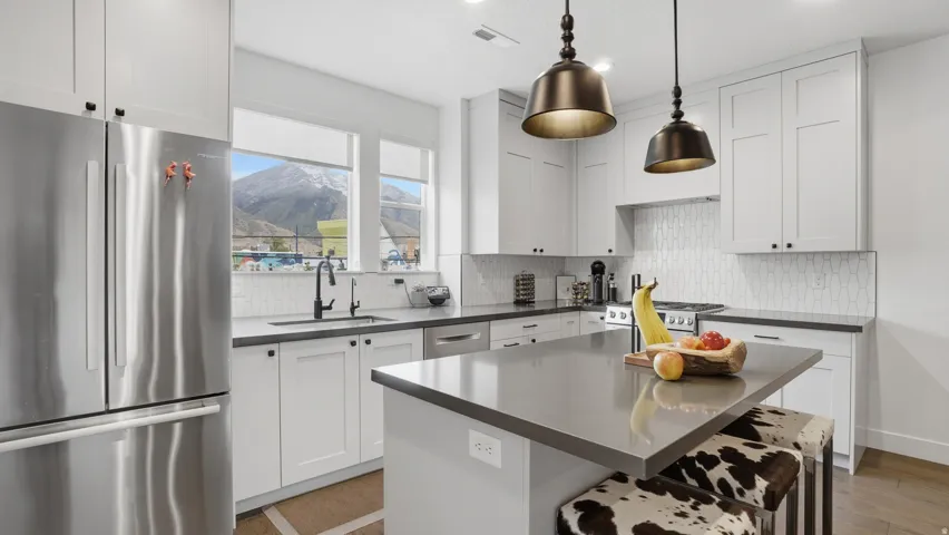 Spacious kitchen featuring white shaker cabinetry, dark countertops, a stainless steel refrigerator, and a tiled backsplash