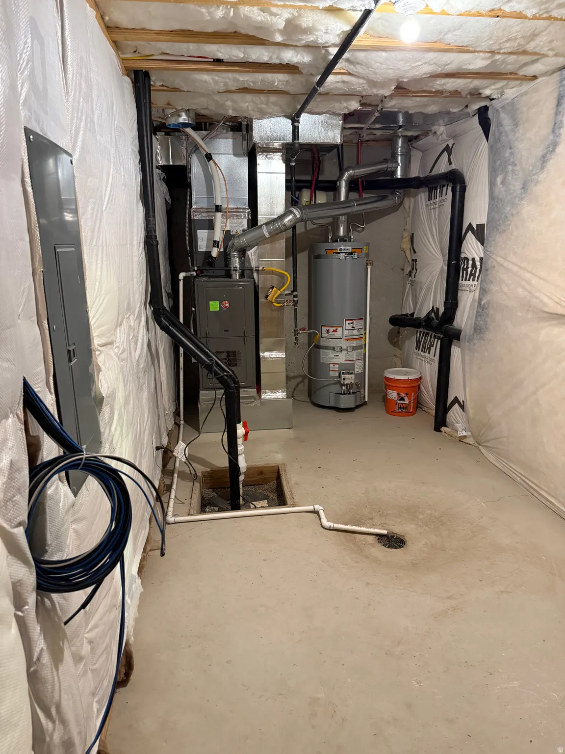 Unfinished basement featuring a concrete floor, exposed ceiling joists with insulation, a water heater, a furnace, and an electrical panel