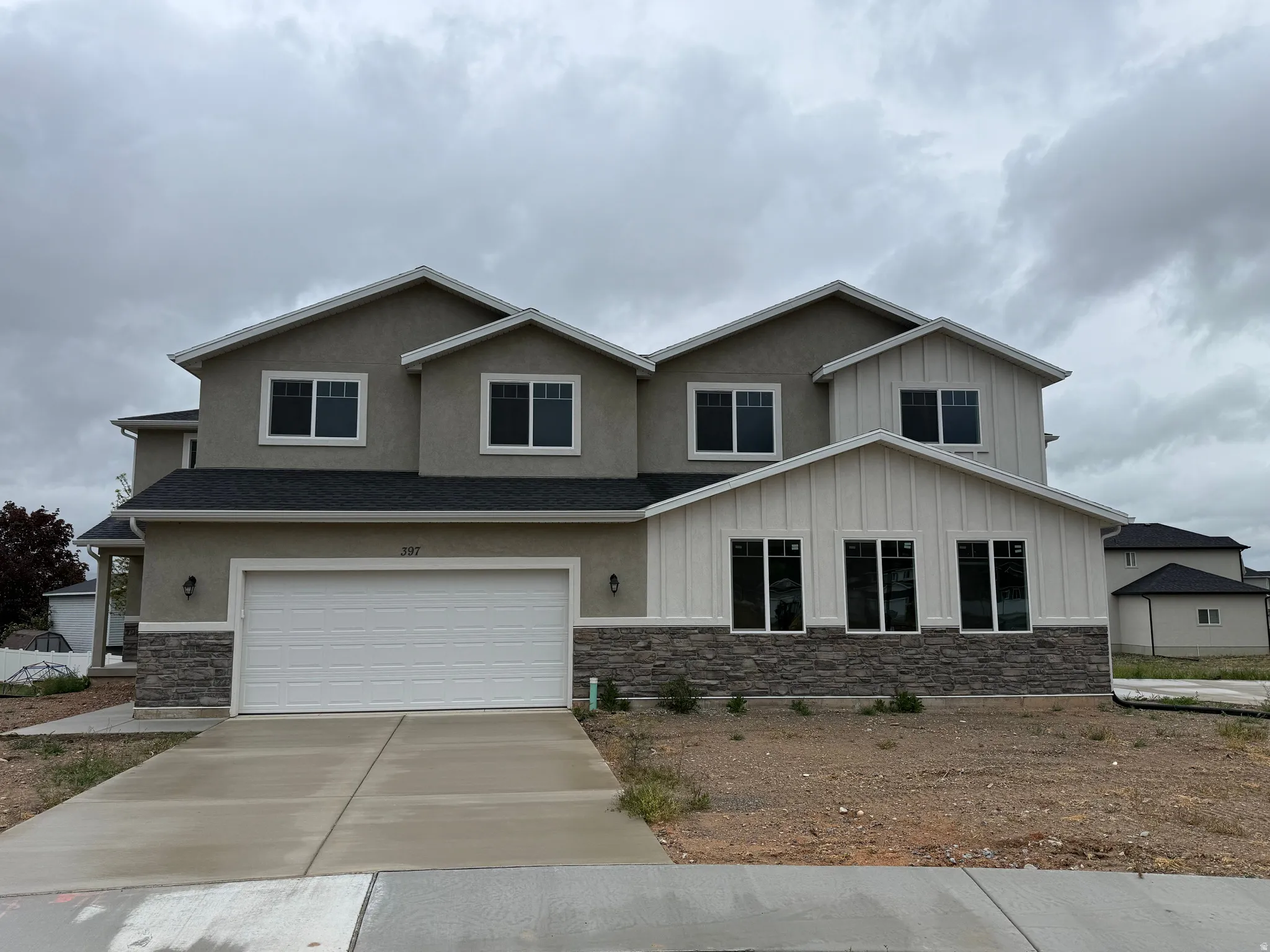 Contemporary multi-level residence featuring a two-tone stucco and board-and-batten facade, dark shingle roofing, and stone veneer accents
