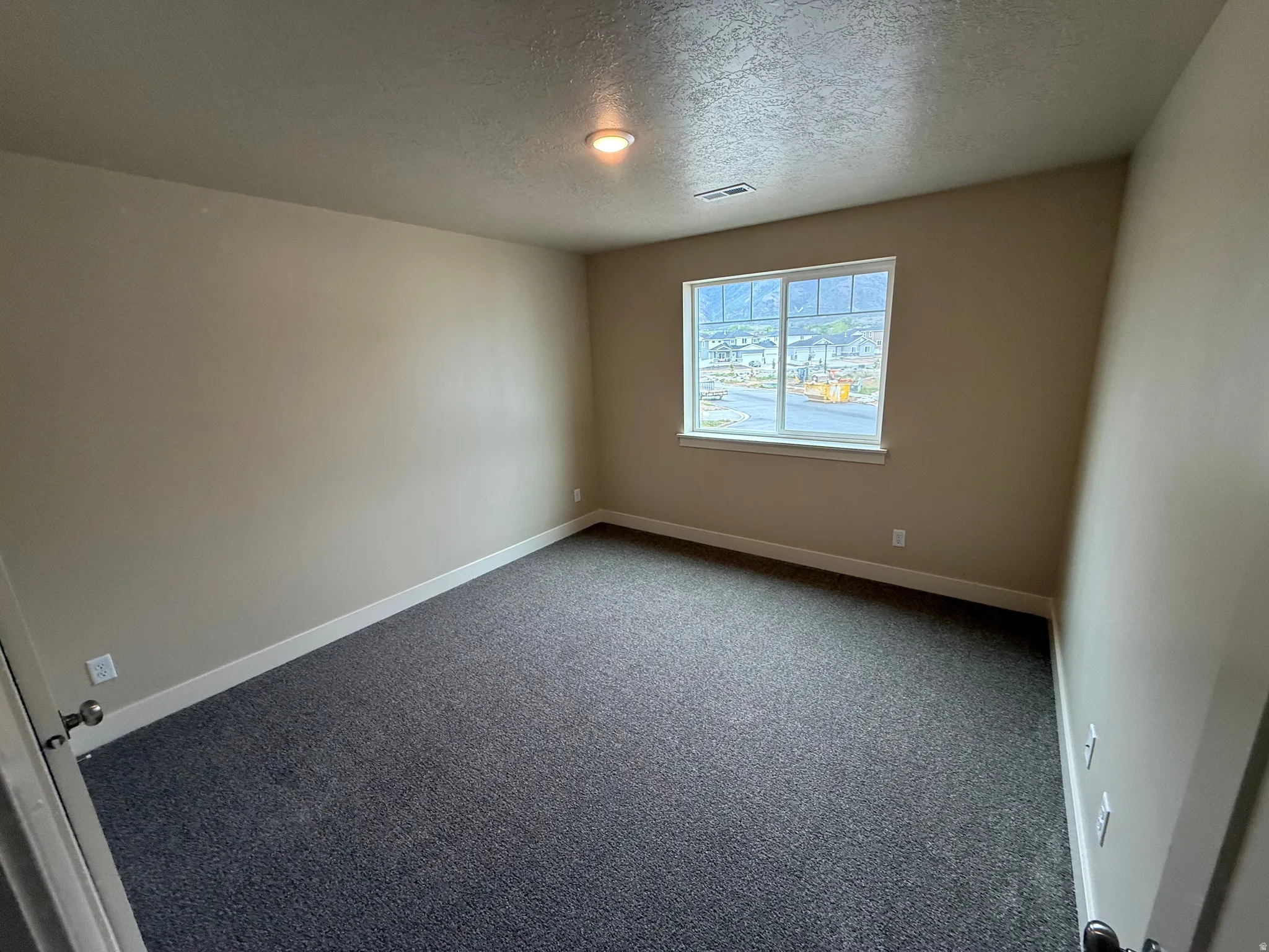 Neutral-toned room featuring a single window with white trim, dark gray carpet, a flush-mount ceiling light, and white baseboards