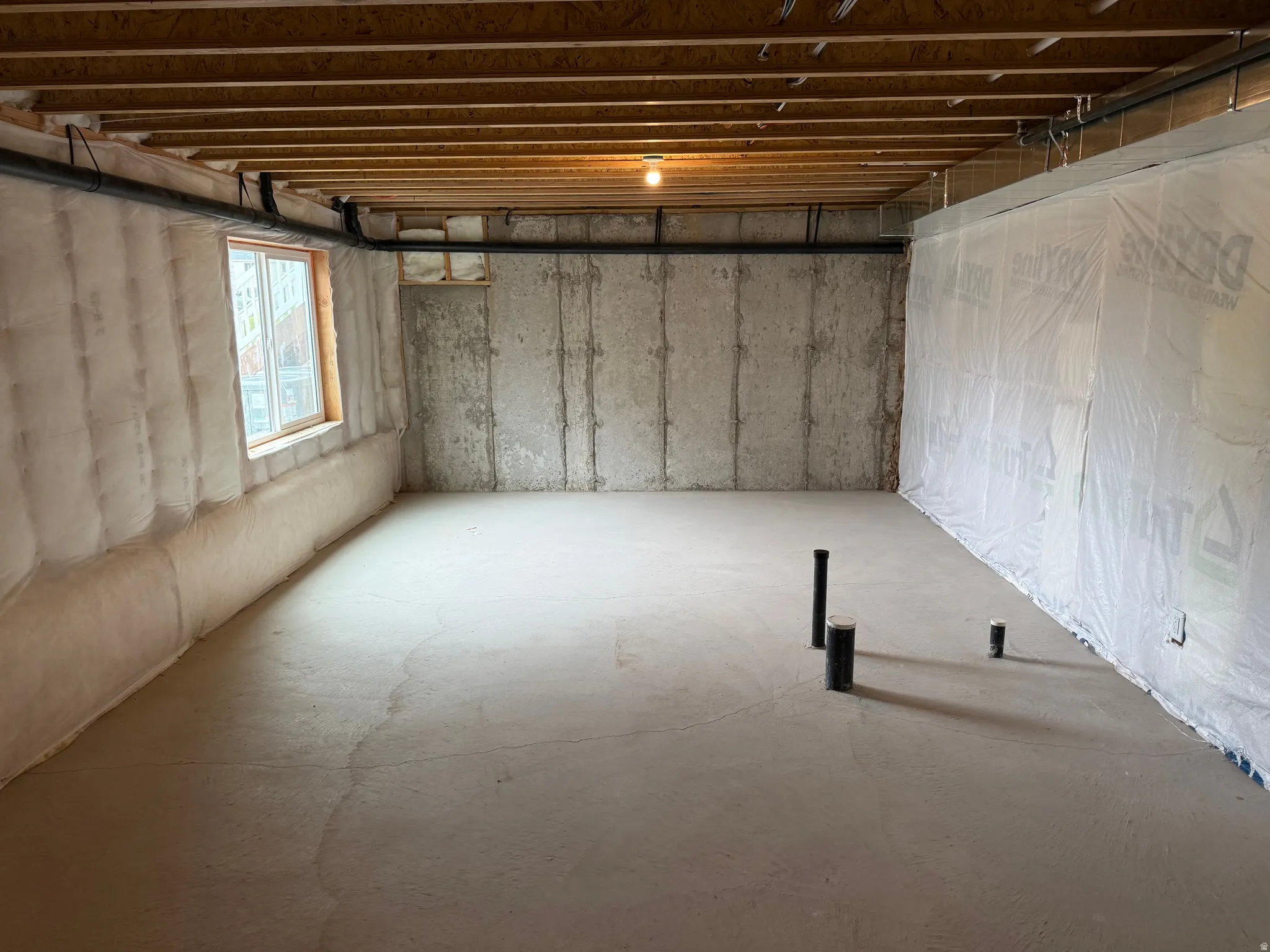 Unfinished basement featuring concrete flooring, exposed wood ceiling joists, and a window providing natural light