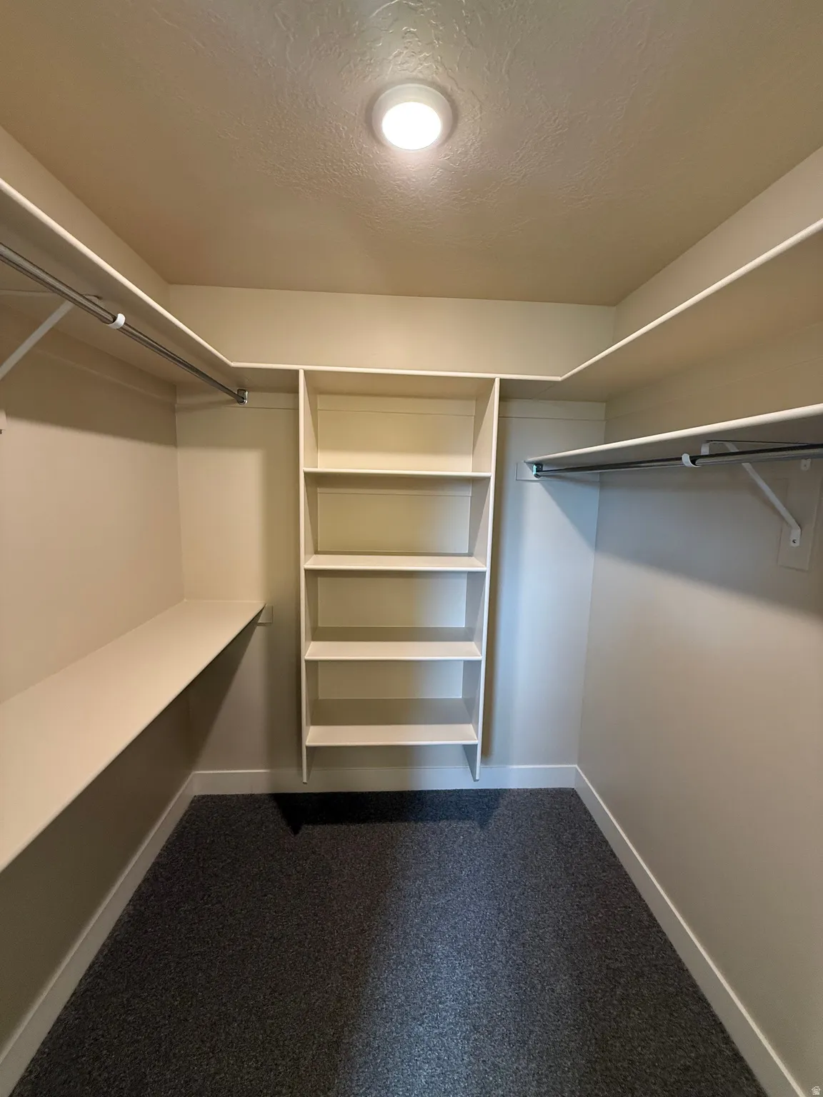 Walk-in closet featuring built-in shelving, hanging rods, and dark gray carpeting