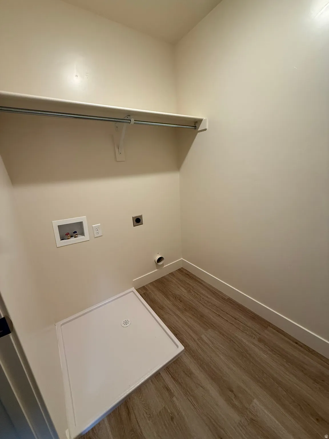 Dedicated laundry area featuring wood-finish flooring, a white utility basin, and a wall-mounted shelving unit with a hanging rod