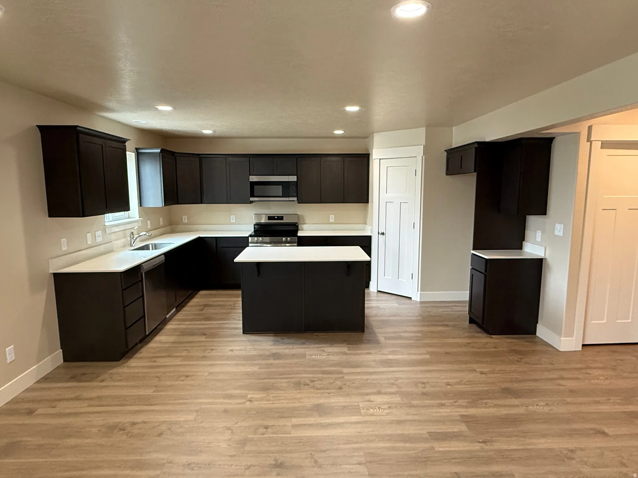 Modern kitchen featuring dark wood-finish cabinetry, light countertops, a central island, stainless steel appliances, and wood-finish flooring