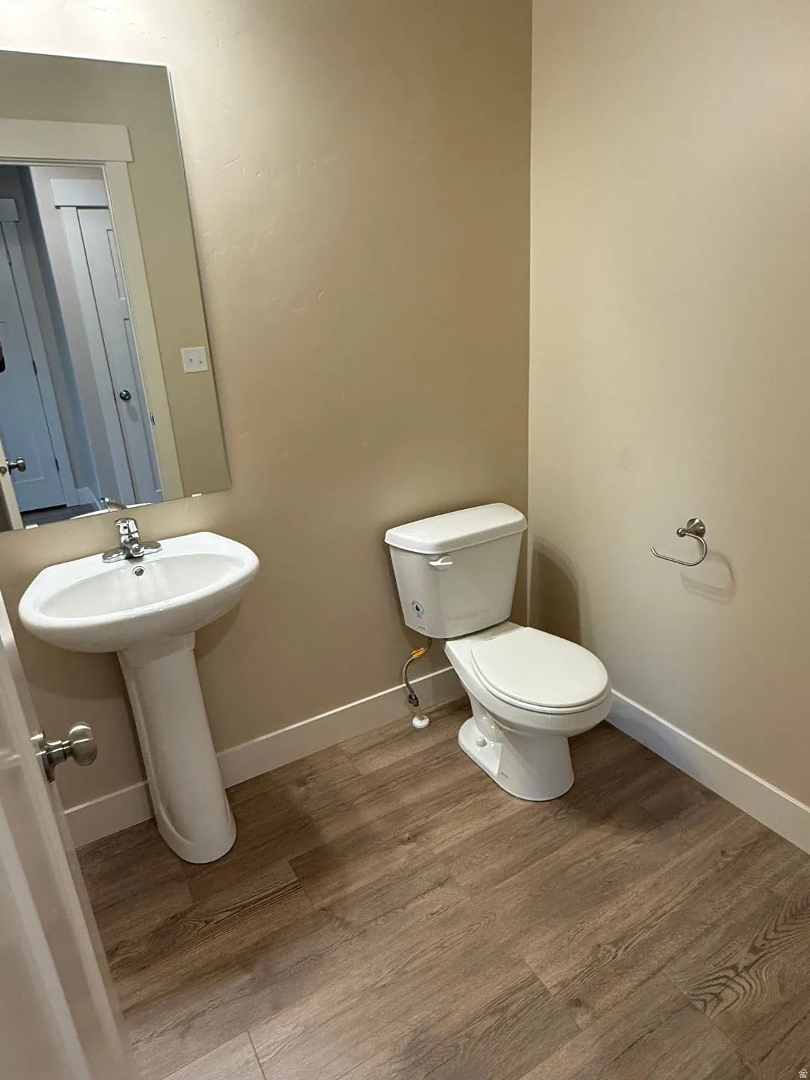 Bathroom featuring a pedestal sink, toilet, rectangular mirror with a framed edge, and wood-finish flooring