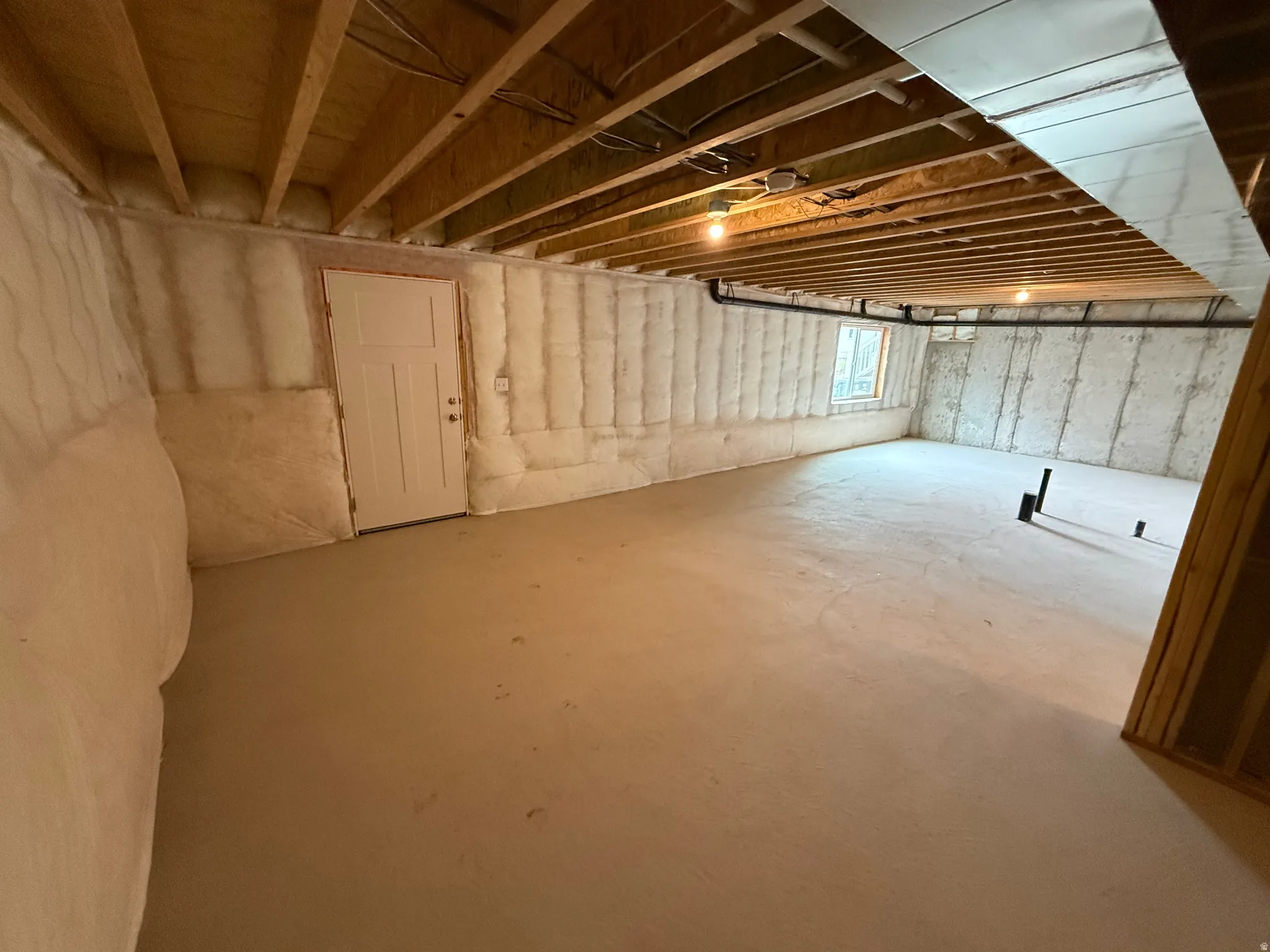Unfinished basement featuring exposed wood ceiling joists, spray foam insulation on perimeter walls, and a concrete floor
