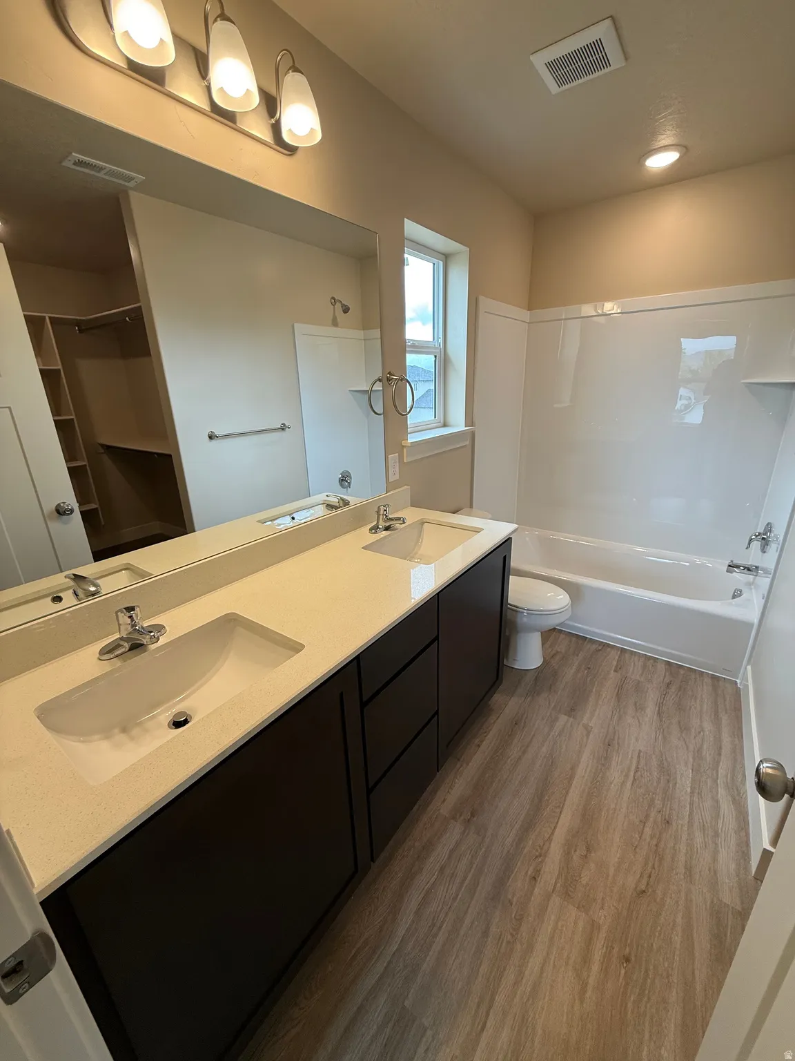 Bathroom featuring a dual vanity with rectangular undermount sinks, stone-finish countertops, dark cabinetry, and wood-finish flooring