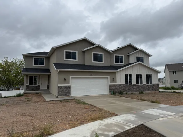 Two-story residence featuring a combination of stucco and vertical siding, stone accents, a two-car garage, and multiple windows