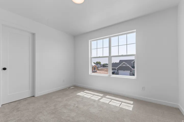 Neutral toned carpeting, contemporary white walls, single overhead light fixture, and a large window with grid pattern