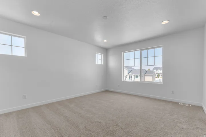 Recessed ceiling lighting, white walls, multiple windows, and neutral carpeting