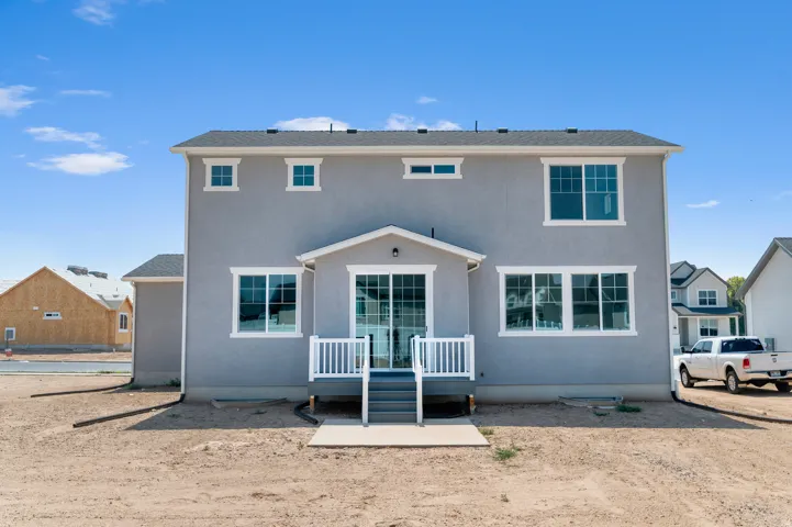 Two-story stucco exterior with multiple windows, a covered deck featuring white railings, and a sliding glass door