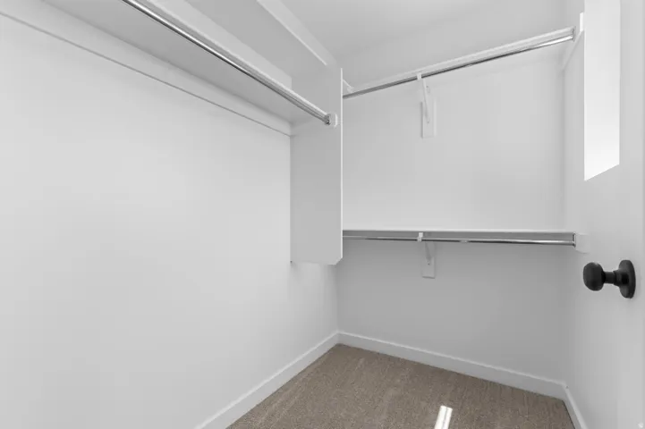 Walk-in closet featuring carpet flooring, built-in shelving, and multiple hanging rods