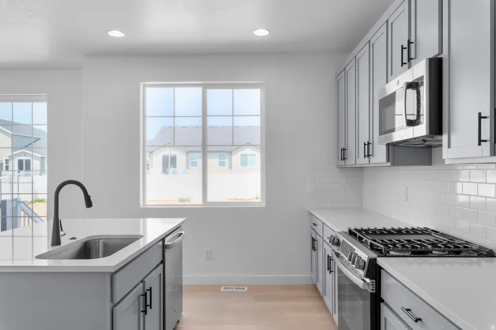 Kitchen featuring light wood-finish flooring, white countertops, gray cabinetry with black hardware, stainless steel appliances, and a white subway tile backsplash