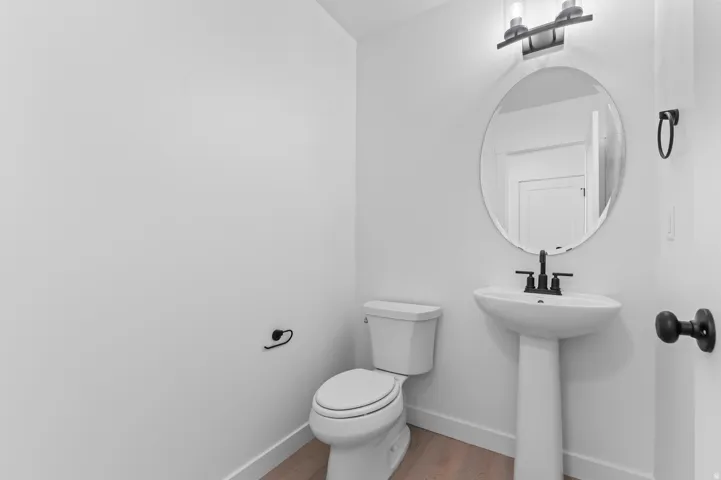 Pedestal sink with a matte black faucet, wall-mounted mirror, and contemporary light fixture