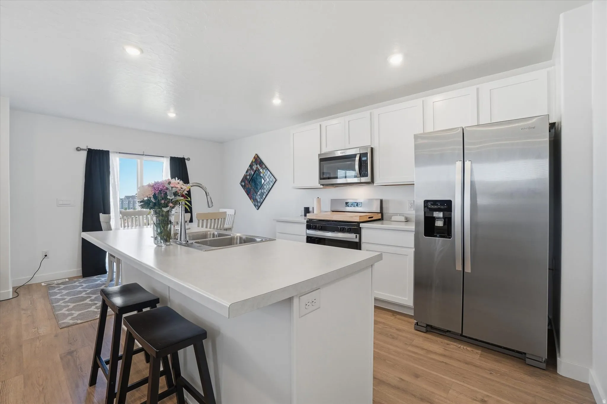 Bright kitchen featuring white cabinetry, stainless steel appliances, wood-finish flooring, a large island with an integrated sink, and recessed lighting