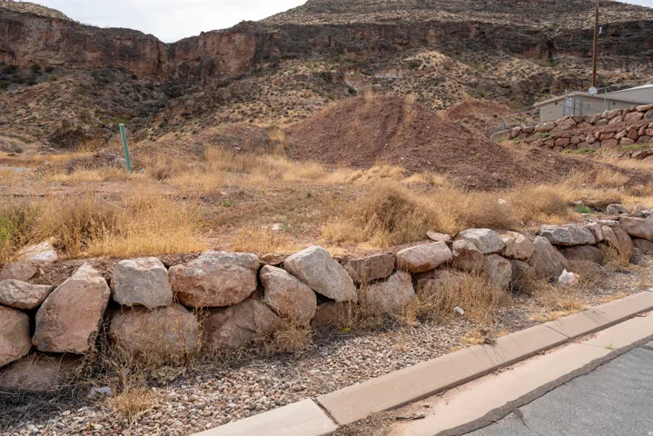 Level lot featuring a natural rock retaining wall, paved road frontage, and mountainous terrain in the background