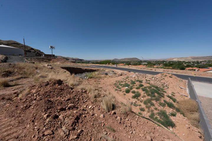 Expansive undeveloped lot with a paved road, distant townscape, and mountain backdrop