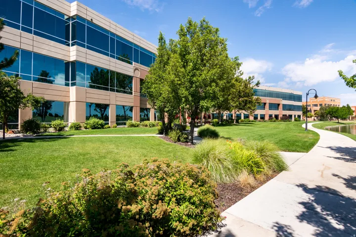 Modern commercial building with reflective glass panels, beige facade, and manicured green lawns