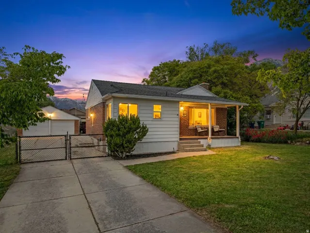 Siding and brick exterior with a covered porch, established front lawn, and a paved driveway leading to a detached garage