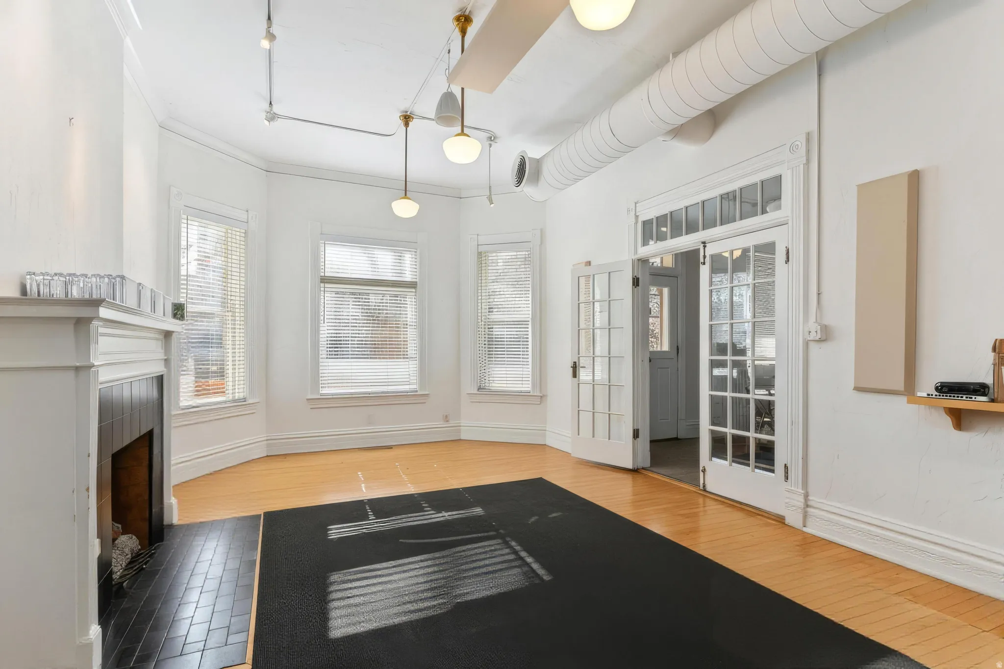 Spacious room featuring light wood-finish flooring, a white mantel fireplace with black tile hearth, and multiple windows