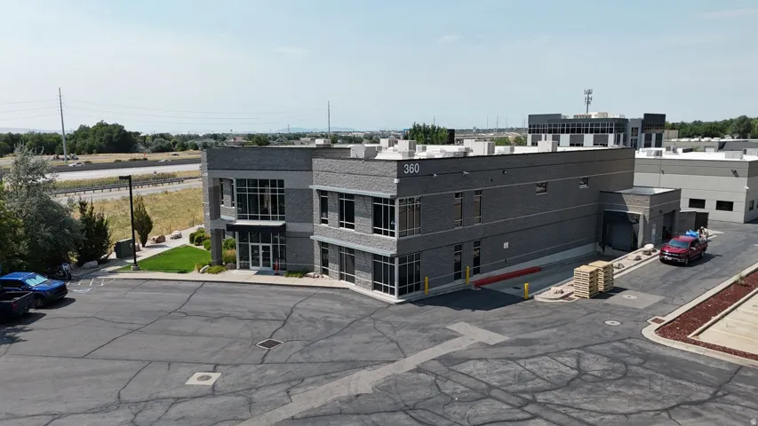 Contemporary commercial building featuring a two-story glass facade, dark gray brick exterior, a loading dock, and an expansive asphalt parking area