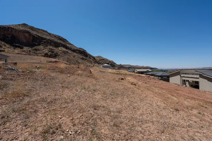 Expansive undeveloped lot with sloping terrain, featuring a backdrop of natural rock formations and a distant mountain range