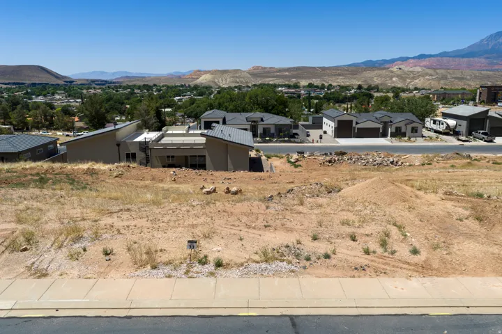 Expansive undeveloped lot featuring a paved roadway, concrete sidewalk, and distant mountain backdrops