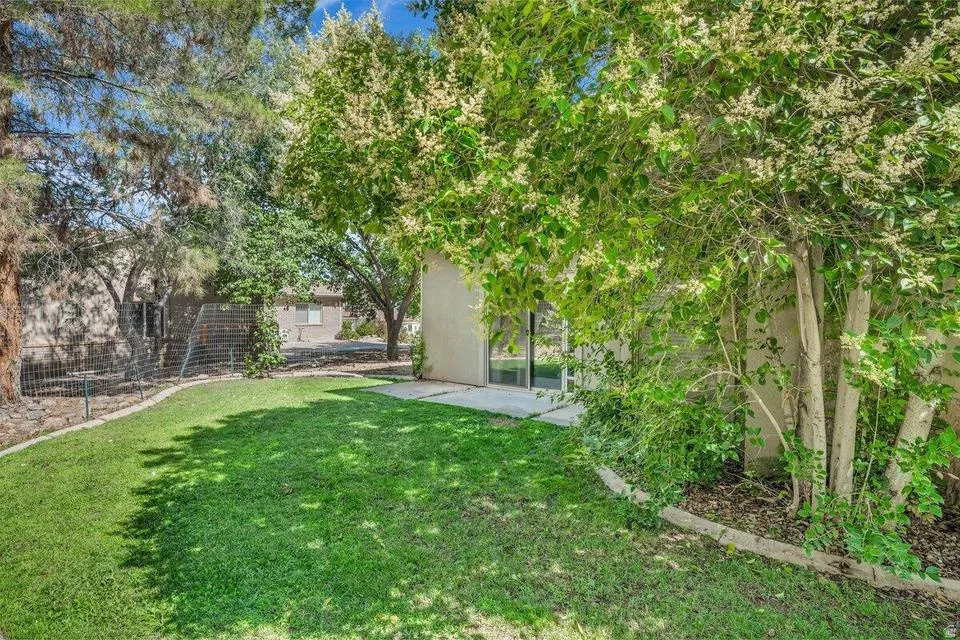 Grassed yard with mature trees, established landscaping, concrete paver path, and a neutral-toned exterior with a large window