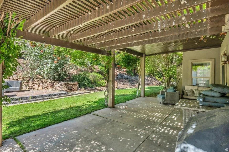 Expansive patio featuring a concrete surface, a slatted wood pergola, and a stone retaining wall