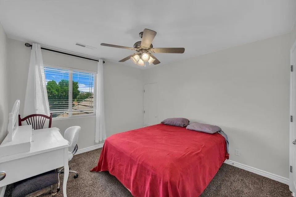 Bedroom featuring a ceiling fan with integrated lighting, a window with horizontal blinds, neutral wall paint, and carpet flooring