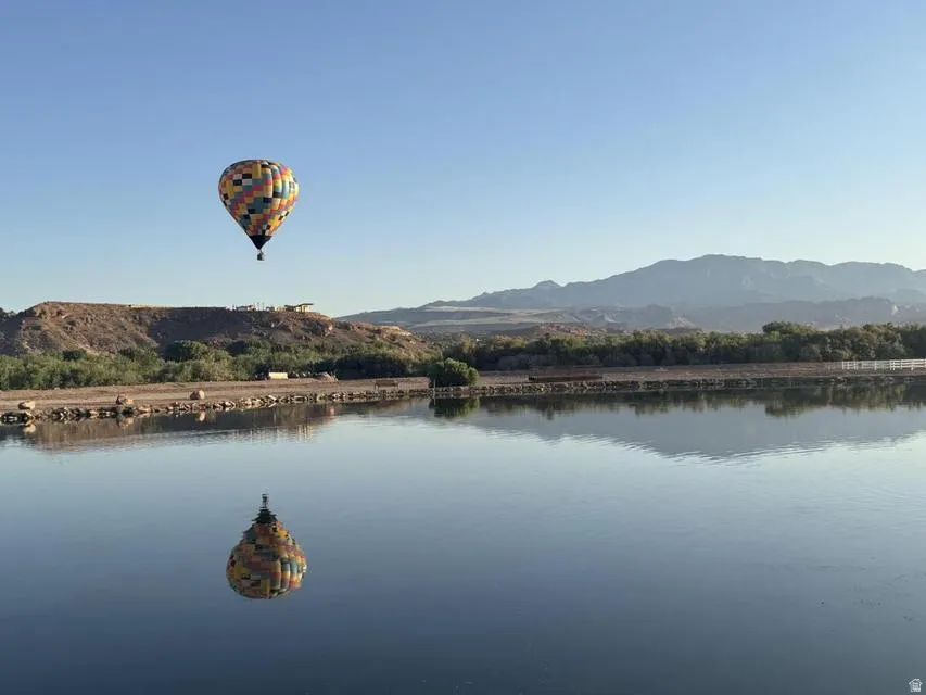 Expansive body of water with a clear reflection, framed by a distant mountain range and a natural, vegetated shoreline