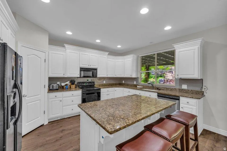 Kitchen featuring white cabinetry, granite countertops, wood-finish flooring, a central island, and recessed lighting