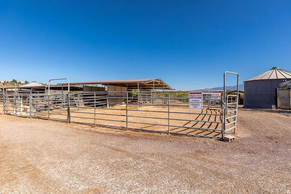 Expansive outdoor arena featuring metal fencing, covered stalls, and a large storage silo