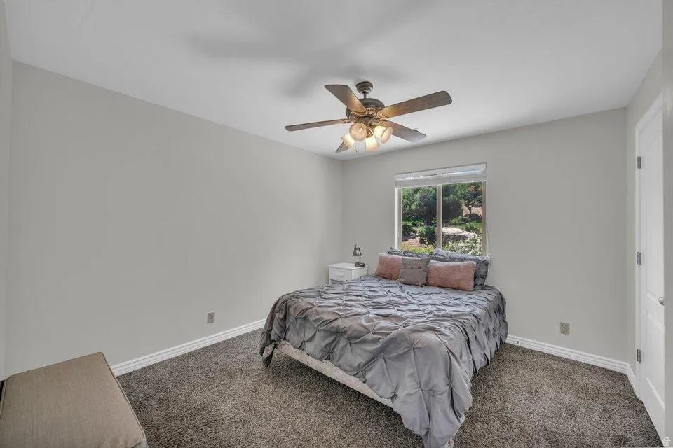 Room featuring neutral wall tones, textured carpet flooring, a ceiling fan with integrated lighting, and a window with a green outdoor backdrop