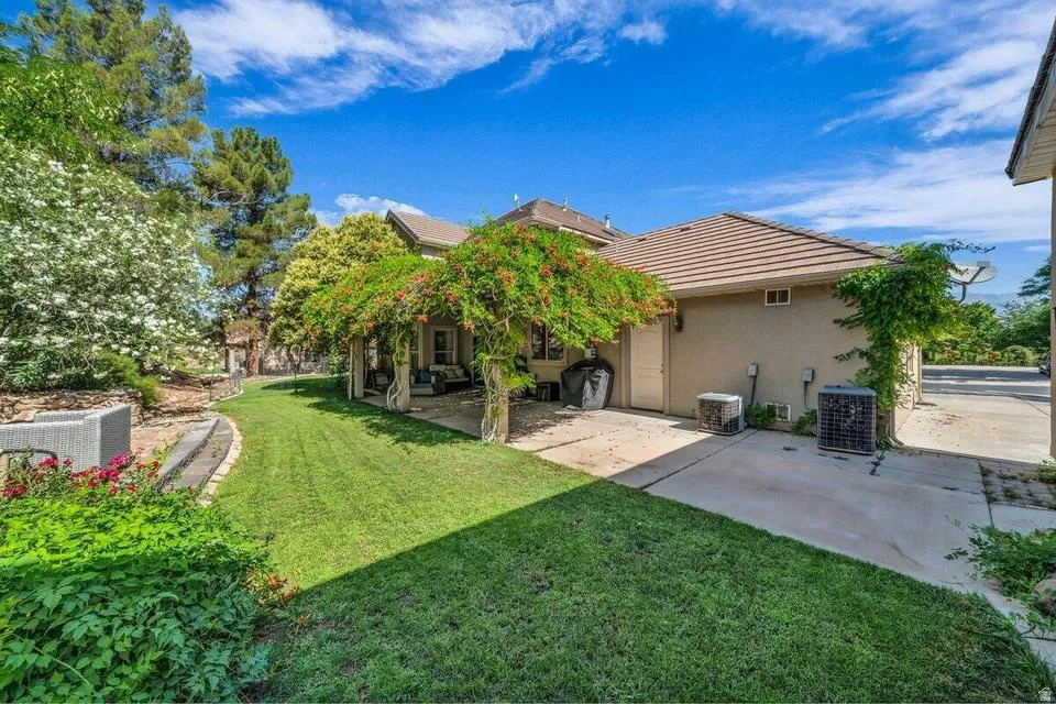 Expansive backyard featuring a manicured lawn, established landscaping, and a covered patio with mature climbing vines