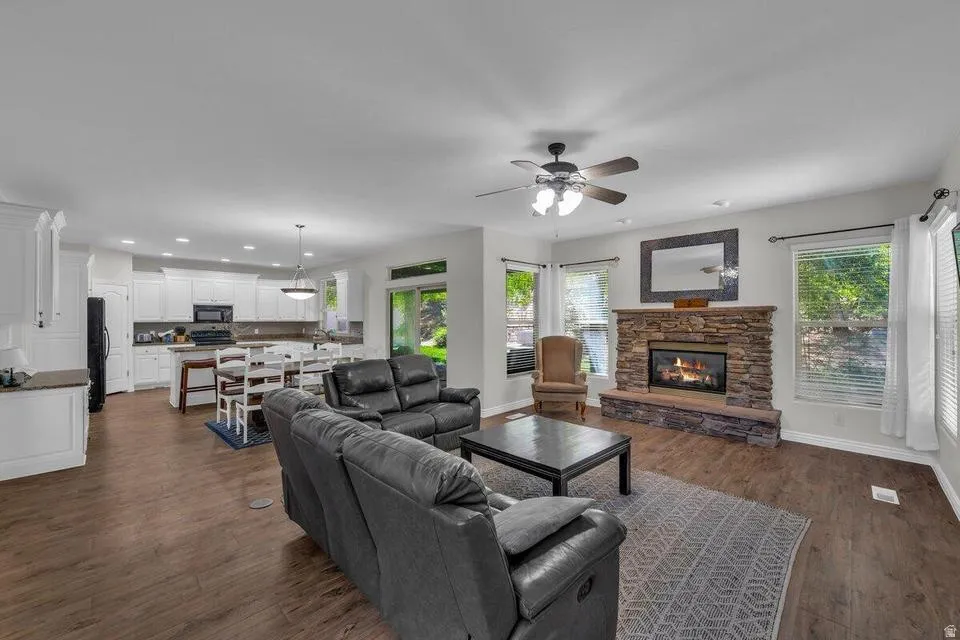 Spacious living area featuring wood-finish flooring, a stone-clad fireplace, and multiple windows