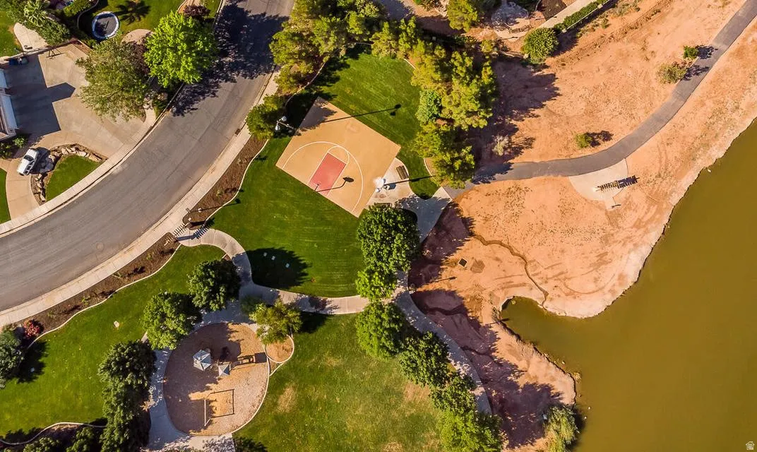Aerial perspective of a curving street bordering a green space with a basketball court, a playground, and a walking path