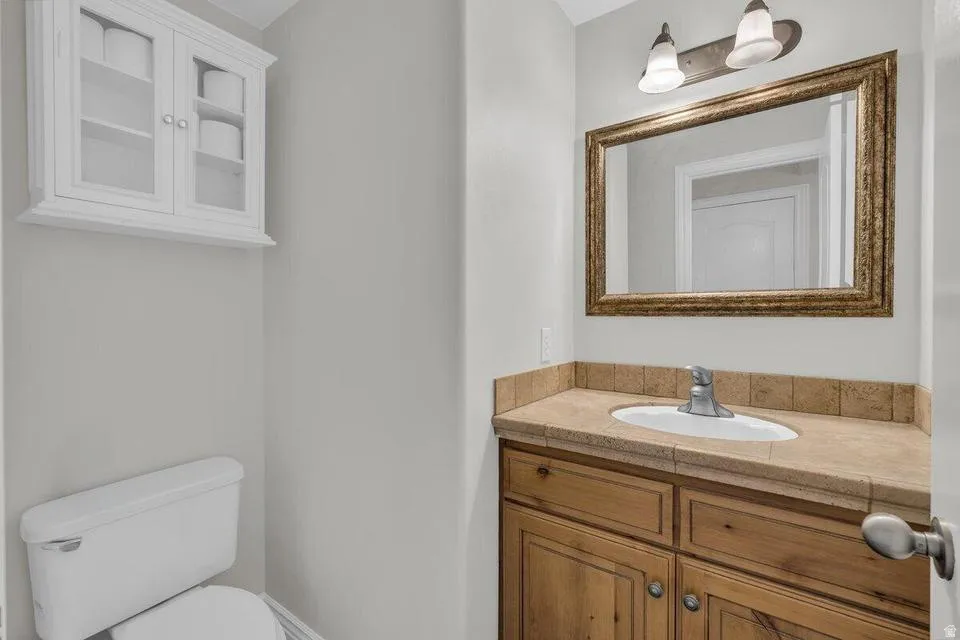 Bathroom featuring a wood vanity with an integrated sink, a light-toned countertop with a tile backsplash, and a framed mirror