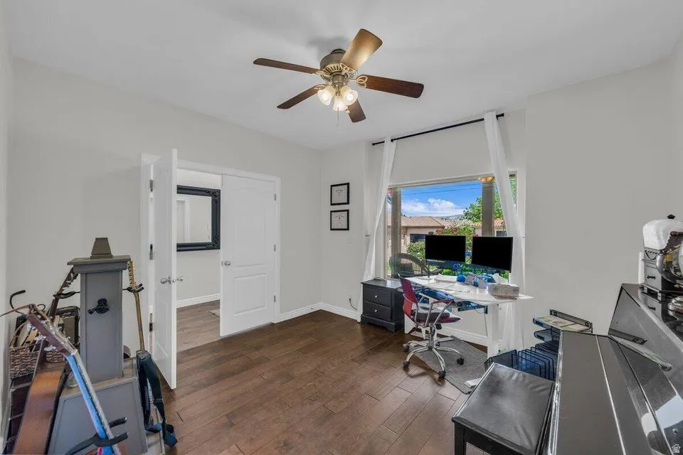Interior room featuring wood-finish flooring, a ceiling fan with light, white walls, and a large window with outdoor scenery