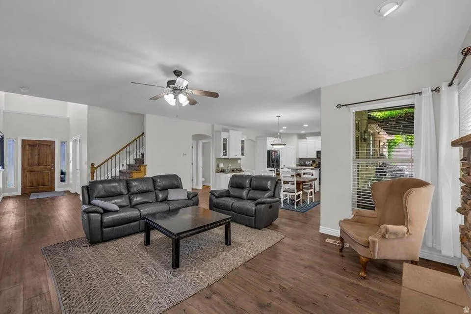 Expansive living area featuring wood-finish flooring, a ceiling fan, and a stone-clad fireplace