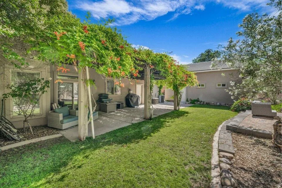 Expansive patio with an overhead pergola, lush green lawn, mature landscaping, and a stone-lined garden bed